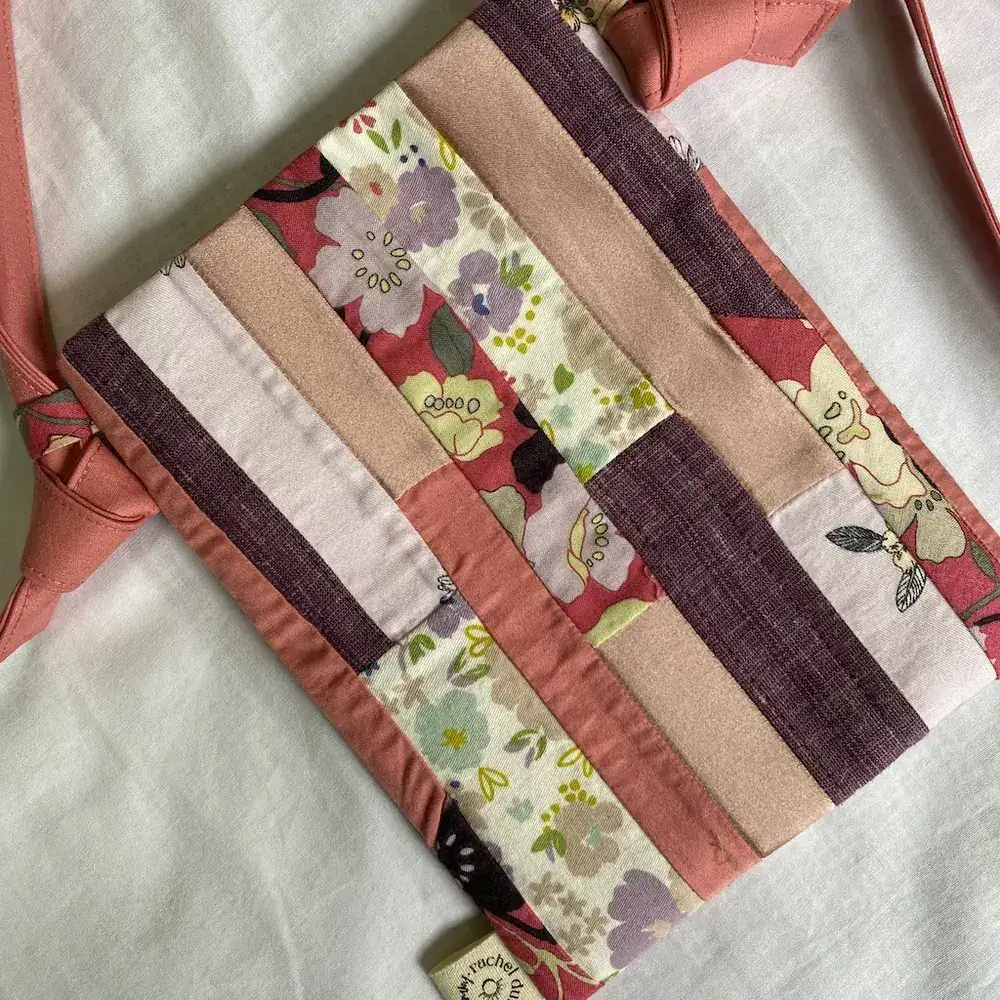 An upcycled patchwork phone bag in blush pink, laid flat on pale linen